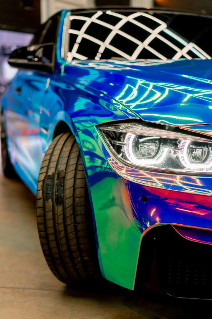Close-up of headlight wheel and bumper of luxury car covered with protective film in chameleon color